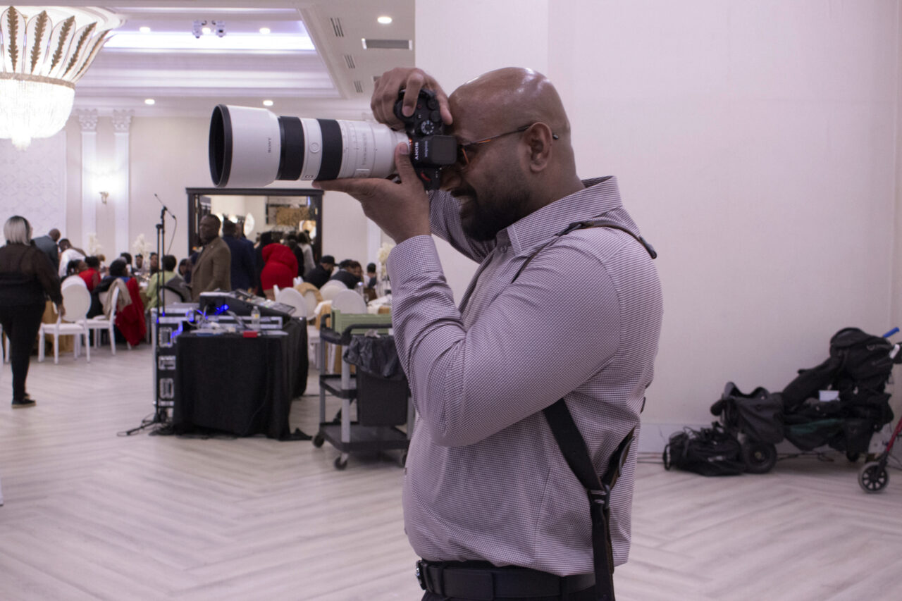Baveen Kana, another event photographer at the event, in action with a large camera lens over his face